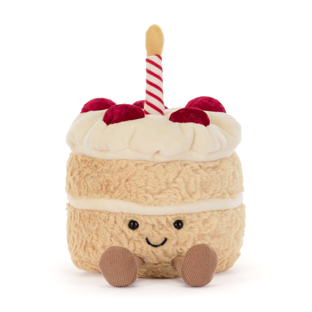 A plush cake toy with cream-colored frosting, red cherries, a red-and-white striped candle, and a smiling face 