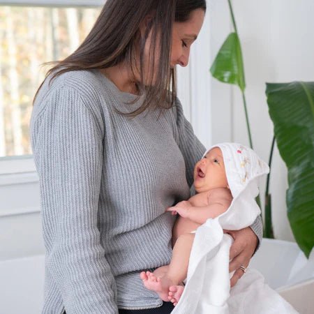 Parent holding baby wrapped in Aden + Anais Essentials Elephant Circus hooded towel after bath