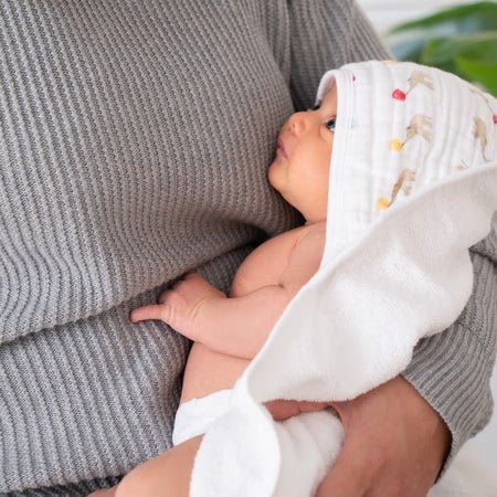 Baby wrapped in Aden + Anais Essentials Elephant Circus hooded cotton muslin towel held by an adult