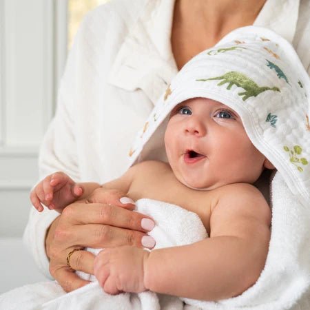 Baby wrapped in Aden + Anais Essentials Dino Jungle hooded towel with dinosaur print held by an adult