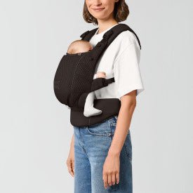 CYBEX Amya Carrier Baby Carriers Almond Beige - Woman using a black baby carrier on a plain background