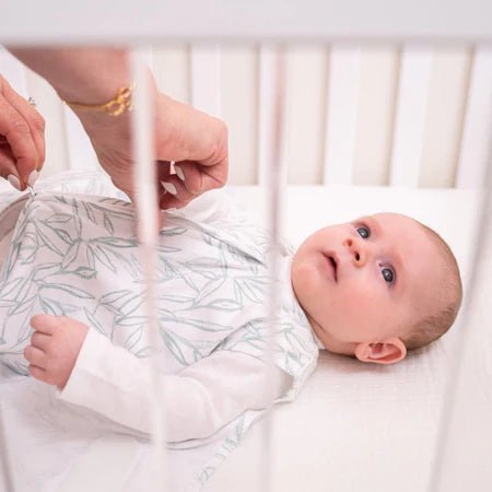 HALO Swaddle 100% Cotton TOG 1.5 Sleepsac Swaddle Small -  Baby lying in a crib with a person adjusting the blanket