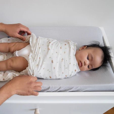 Baby resting in HALO cotton SleepSack Swaddle on changing table