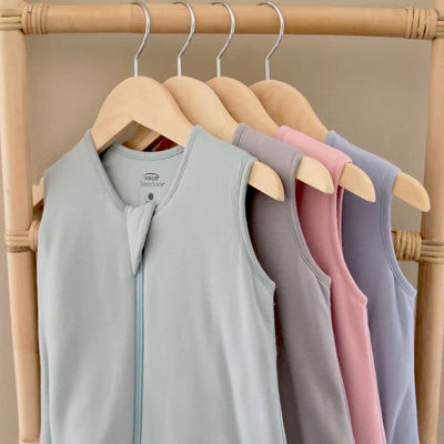Four sleeveless shirts in gray, pink, and purple hanging on a wooden rack.