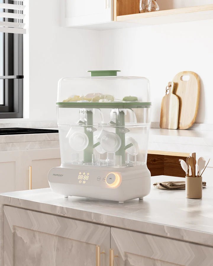 Momcozy 3 Layers Fast Bottle Sterilizer and Dryer with transparent lid displayed on a marble kitchen countertop.