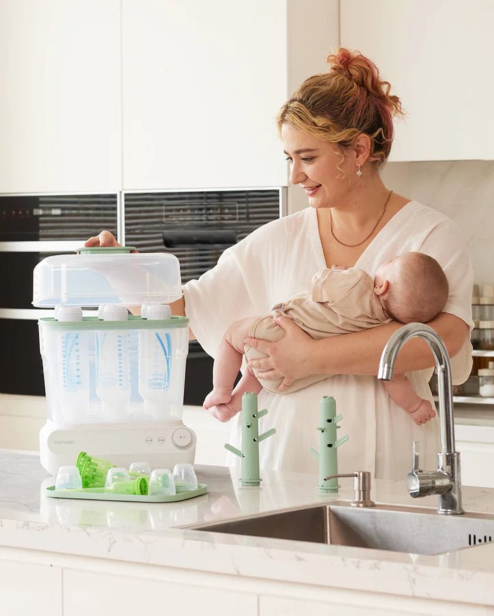 Momcozy 3 Layers Fast Bottle Sterilizer and Dryer used in a modern kitchen with parent holding a baby nearby.