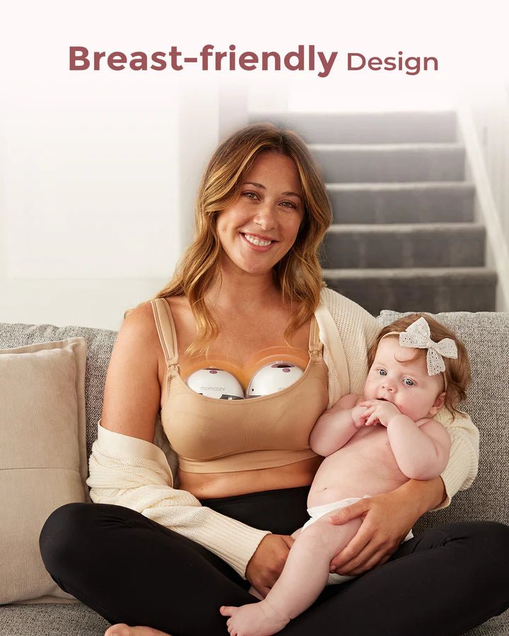 Parent holding a baby while wearing the Momcozy M5 Smart Hands-Free Breast Pump in a comfortable home setting.