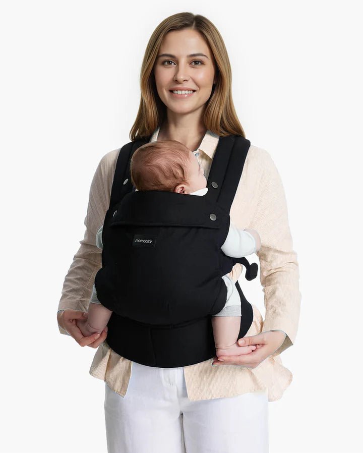 Momcozy Baby Carrier worn by a mom holding her baby, featuring ergonomic comfort for newborn to toddler carrying