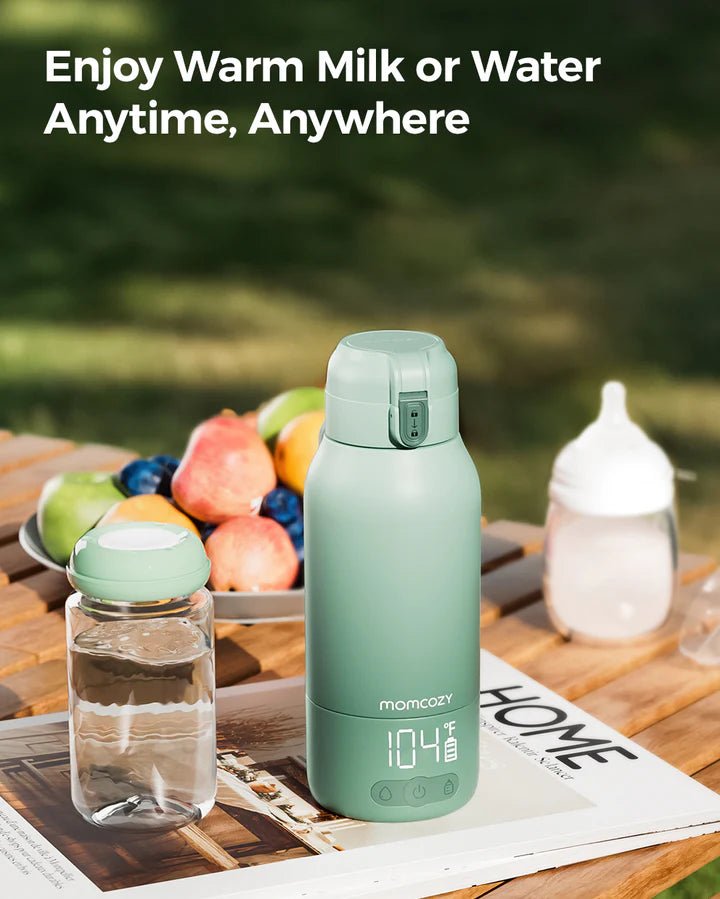 Momcozy portable breast milk and water warmer with digital temperature display shown on a kitchen table with fresh fruit.