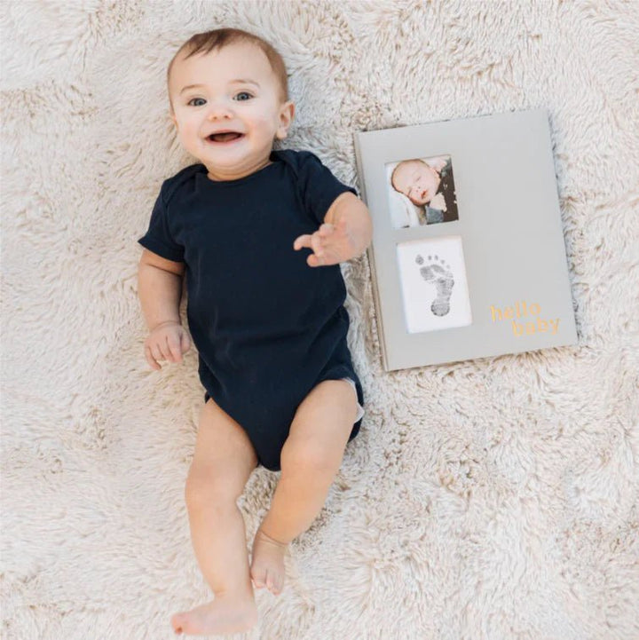 Pearhead Hello Baby Linen Baby Book - Baby next to a photo album with baby photos and prints.