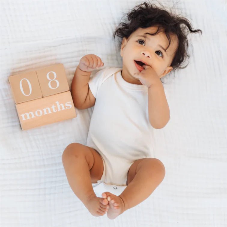 Pearhead - Natural Wooden Milestone Blocks -  Baby in a white onesie with '08 months' blocks 